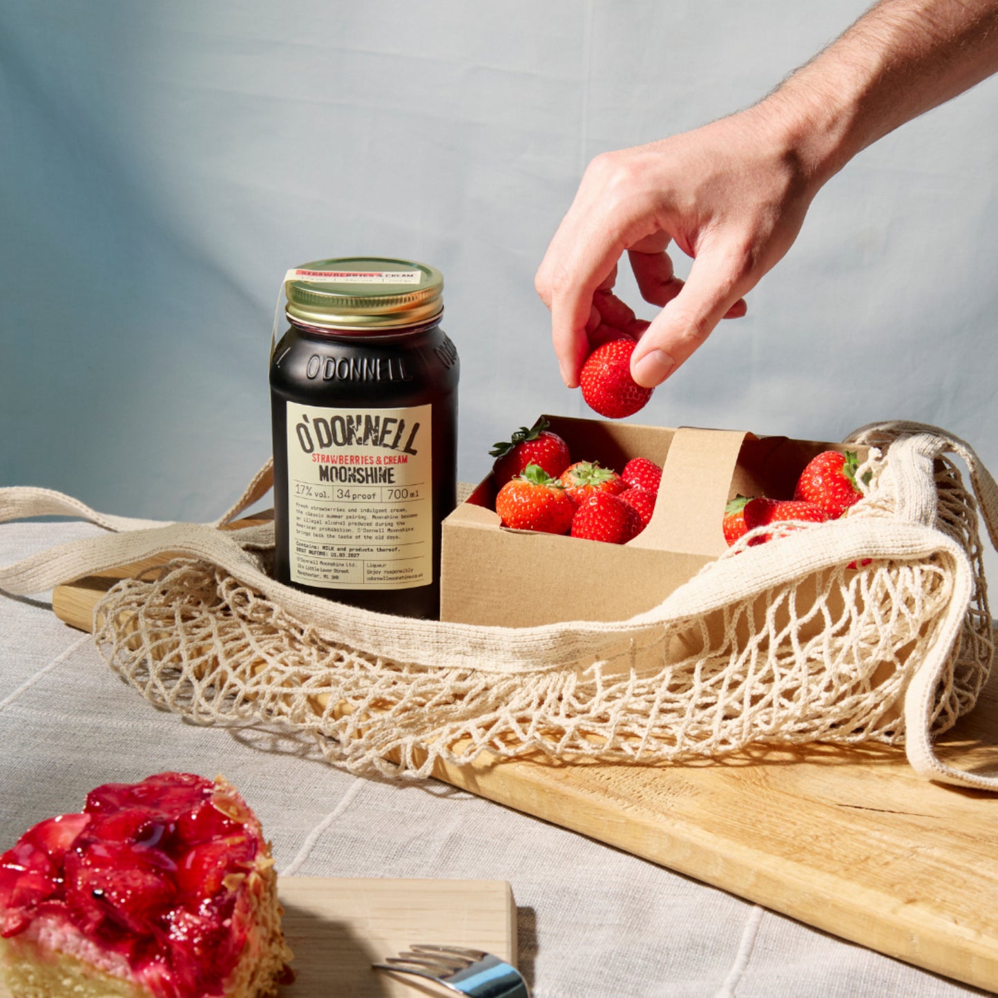 aardbeien & roomlikeur op een blauwe achtergrond met een hand die aardbeien plukt