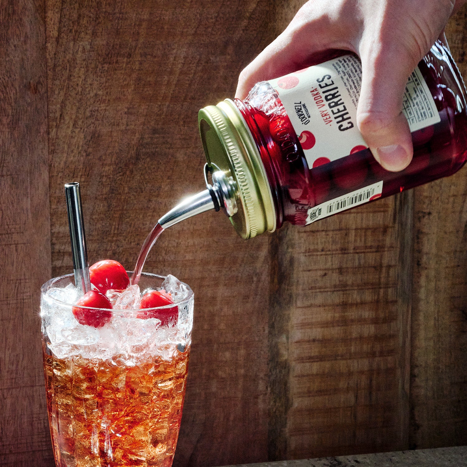 Met de hand schenken van Very Vodka Cherries in een glas ijsdrank met kersen op een houten achtergrond
