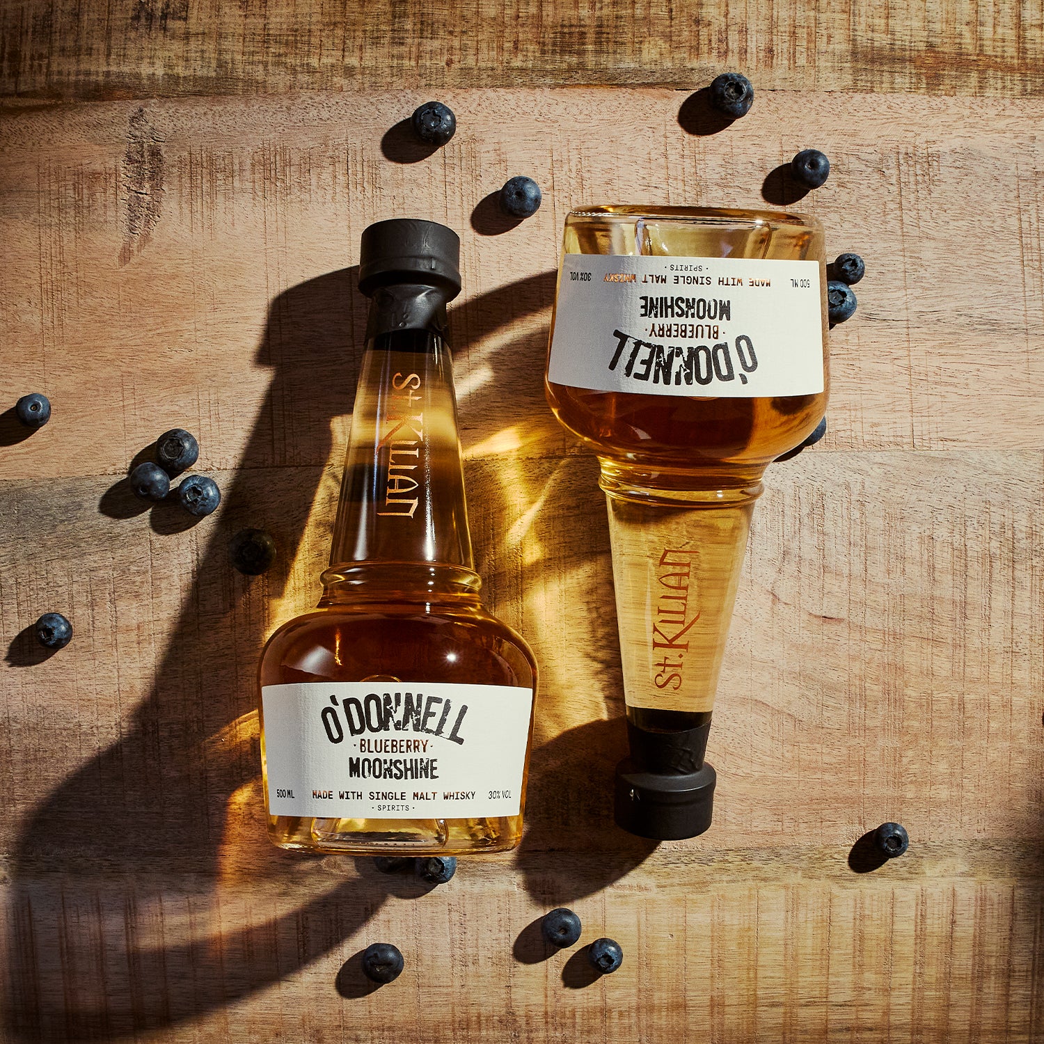 Twee O'Donnell bosbessen moonshine x whisky tegen een zwarte achtergrond en omringd door bosbessen
