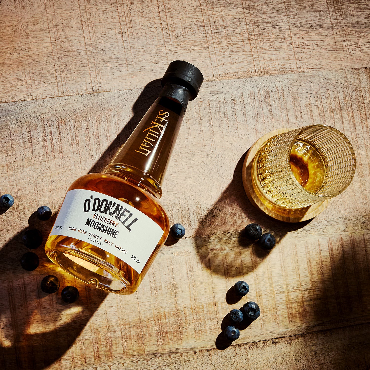 Een O'Donnell bosbessen moonshine x whisky op een tafel met een tumblerglas en bosbessen
