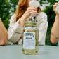O'Donnell Moonshine vlierbessenlikeur in een Mason Jar, met op de achtergrond een groep mensen die ervan genieten als cocktail.